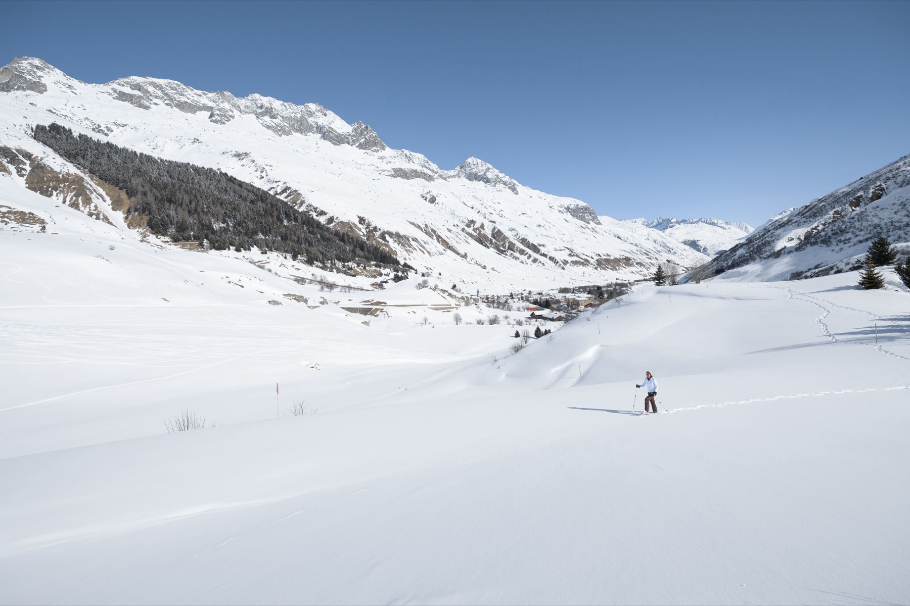 A snowshoer crossing a wide, sunny snowfield in the Urseren Valley near Realp
