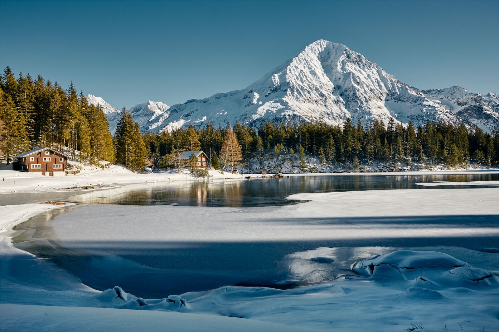The frozen Arnisee with wooden chalets on its shore and a snowy peak beyond