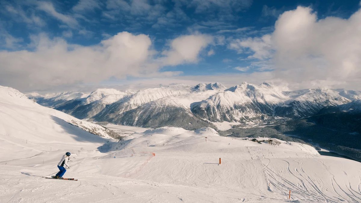 A skier on a wide Corviglia piste with the Engadin's lakes and peaks below