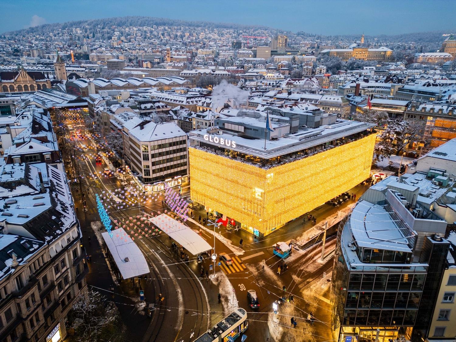 The Globus department store glowing among snowy Zurich rooftops