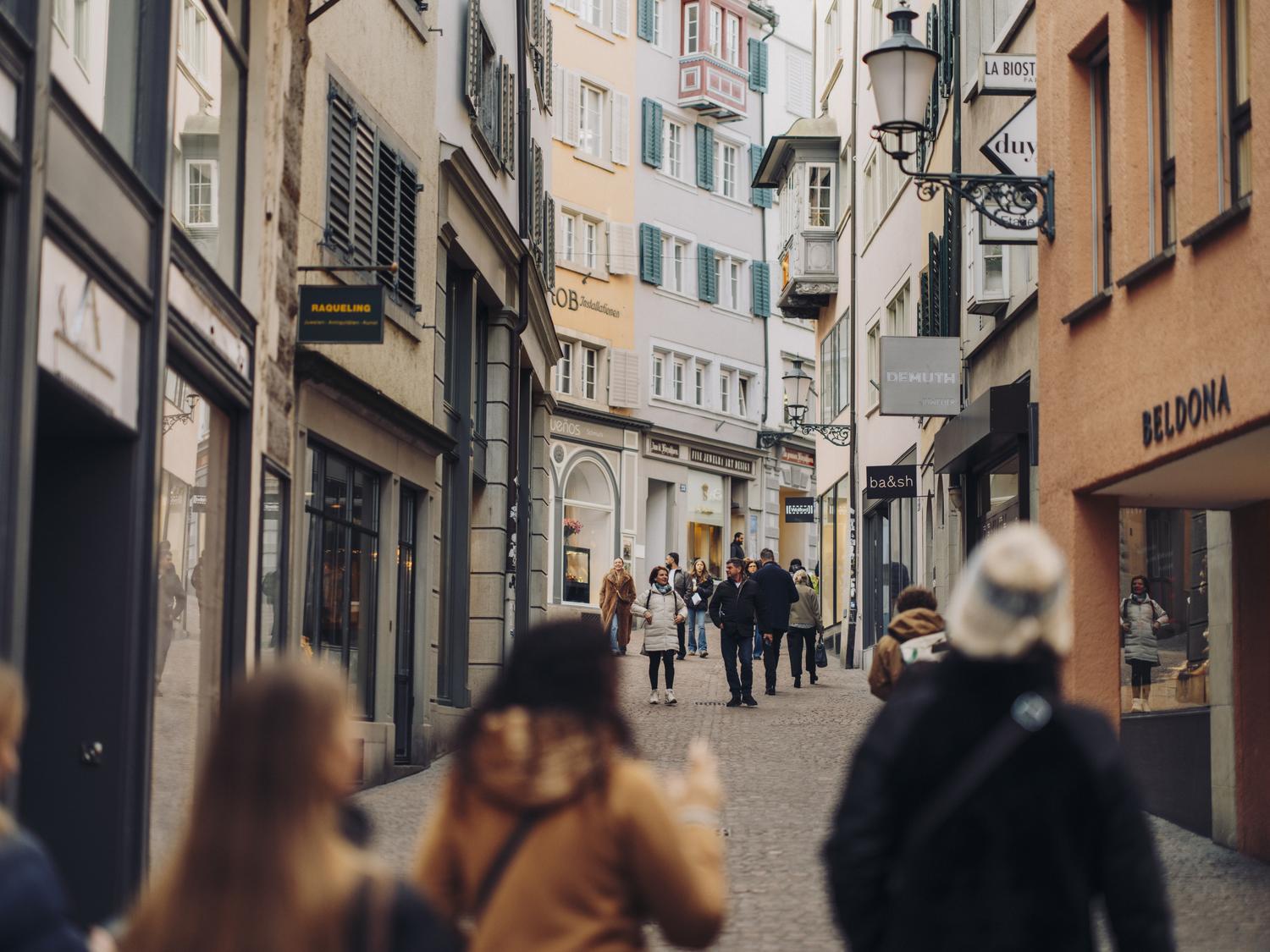 Shoppers strolling a cobblestone Old Town lane lined with boutiques and painted facades