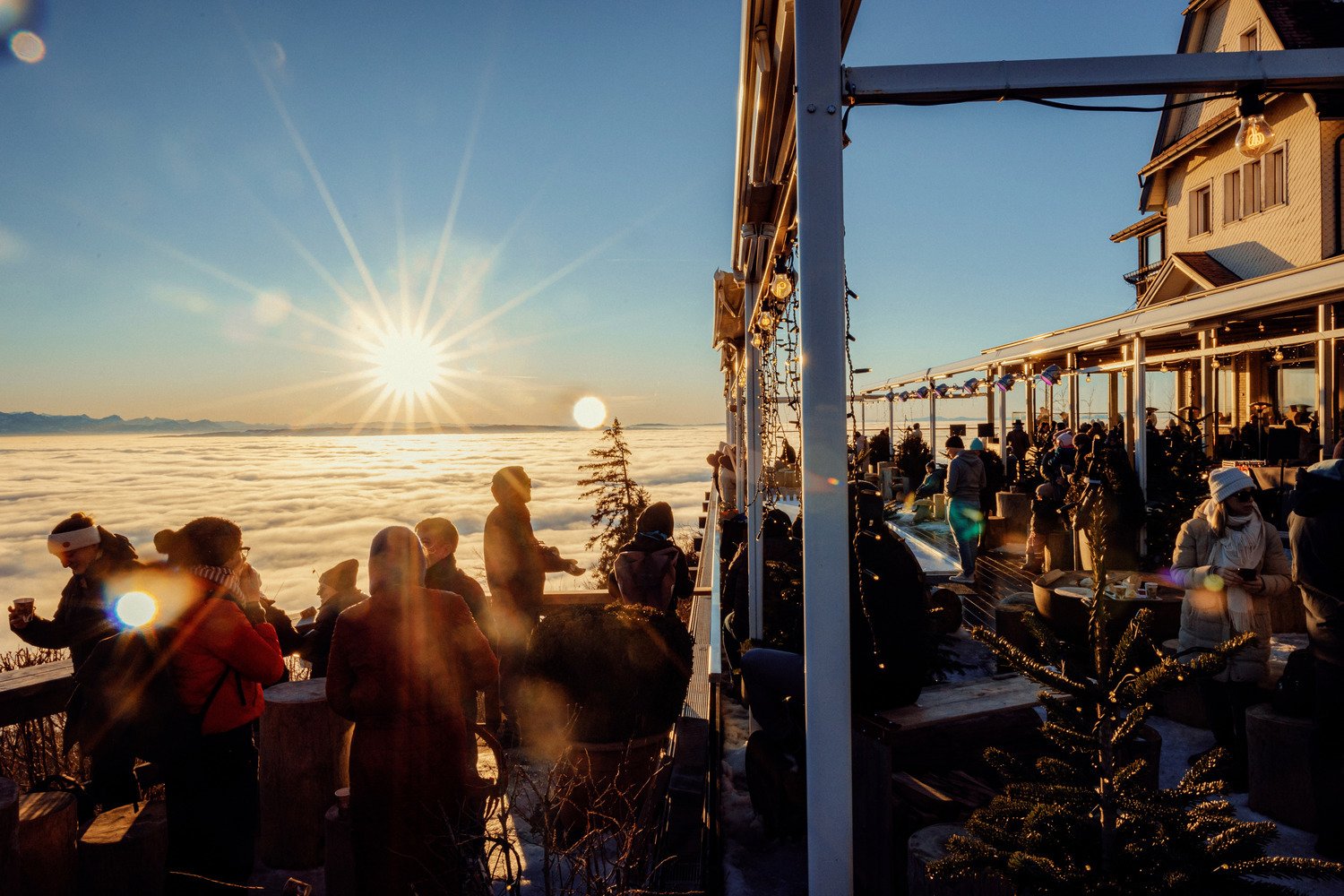 People on the Uto Kulm terrace watching the sun set over a sea of fog