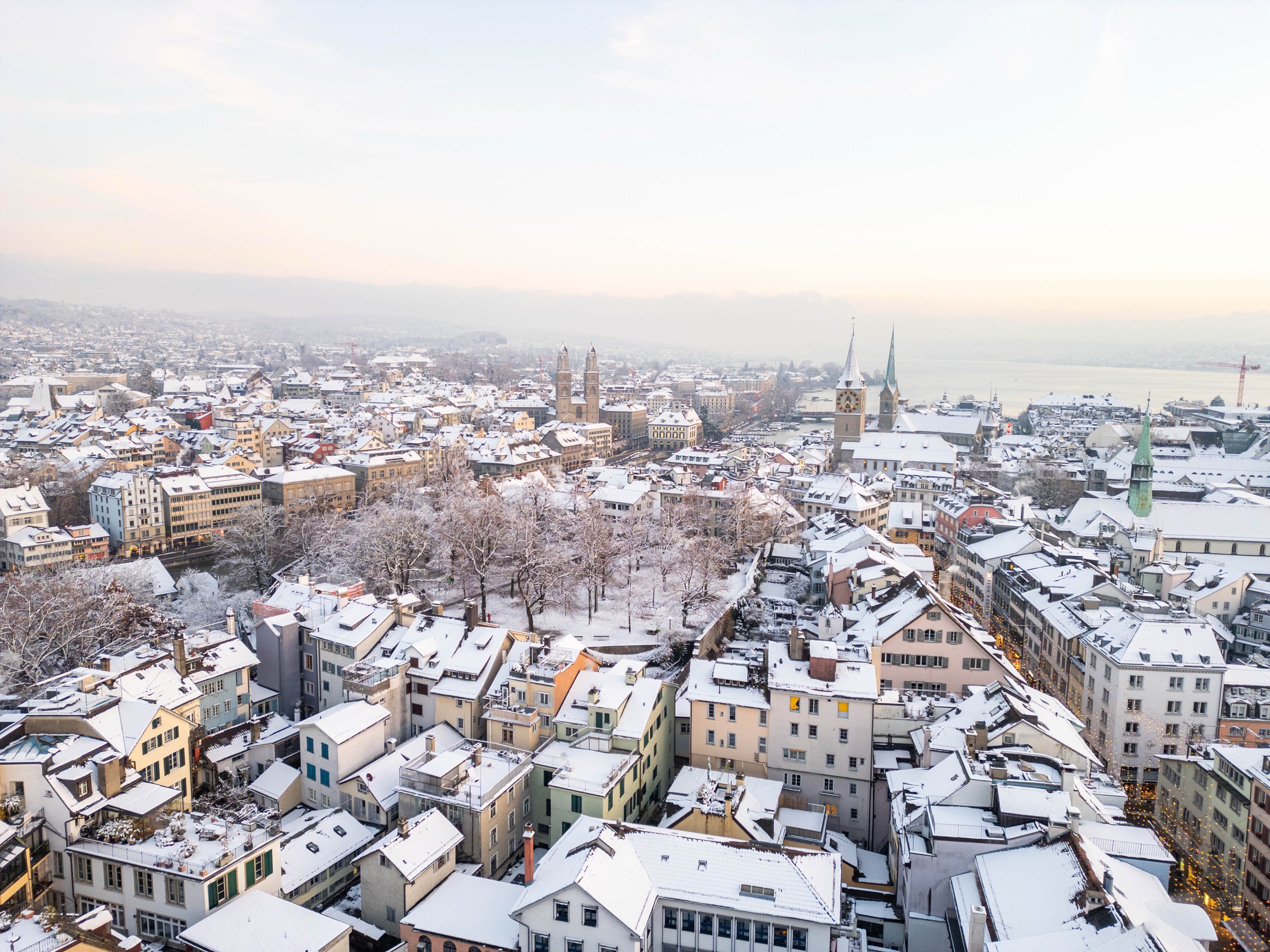 Snow on the rooftops of Zurich's Old Town, with the Grossmünster towers and the lake beyond