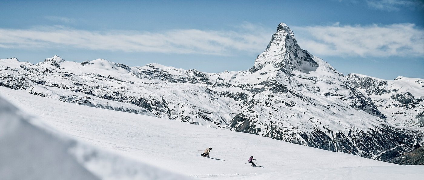 Two skiers carving down a run beneath the Matterhorn