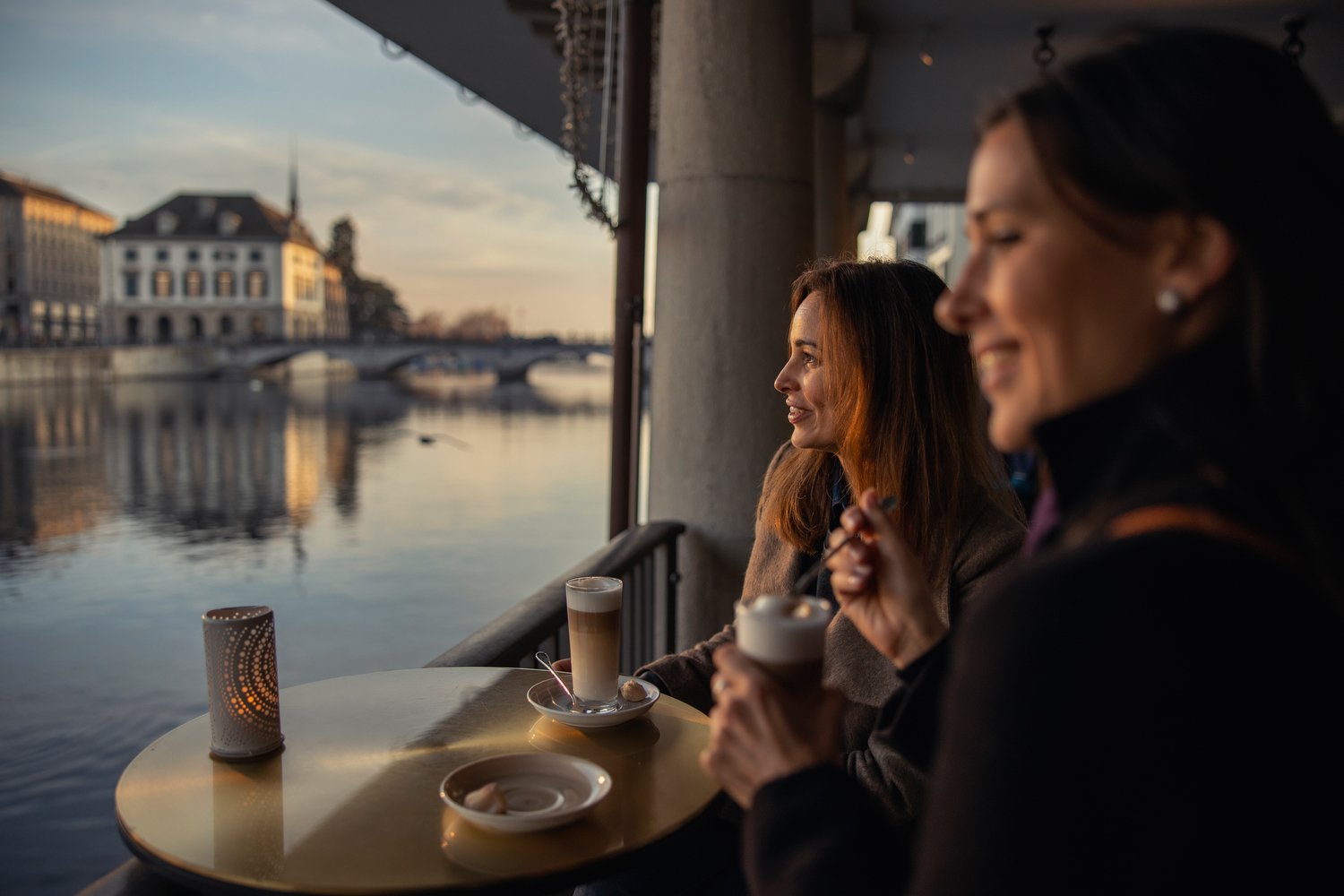 Two friends with warm drinks on a terrace over the Limmat at sunset