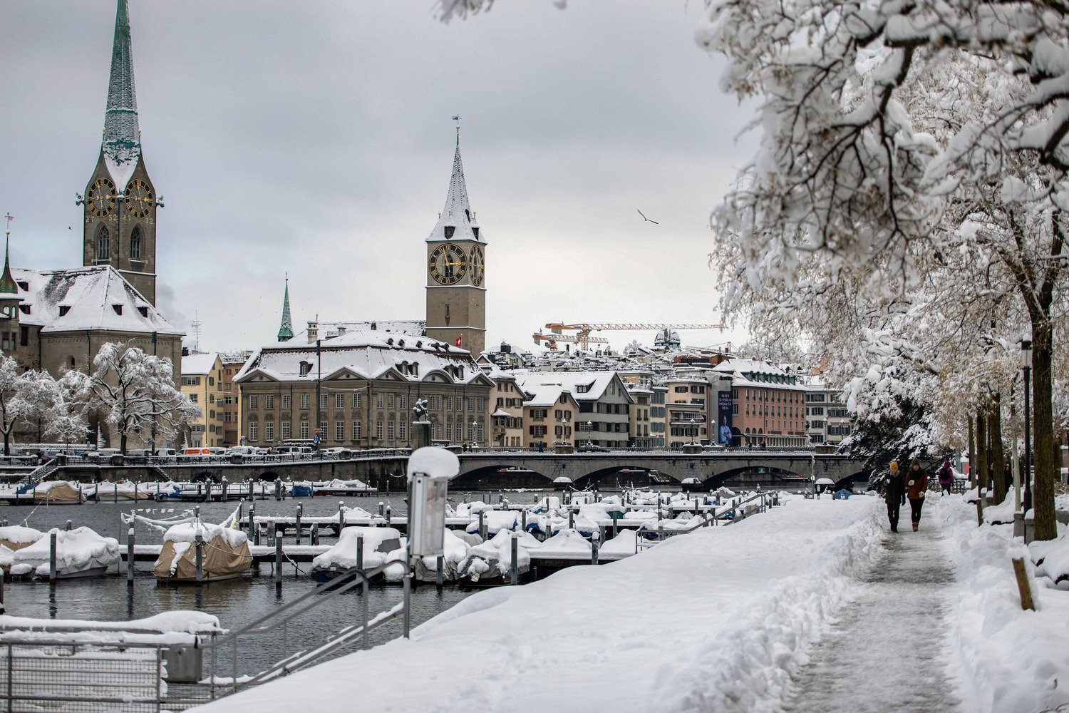 A snowy riverside walk on the Limmatquai, with the Fraumünster and St. Peter's across the water