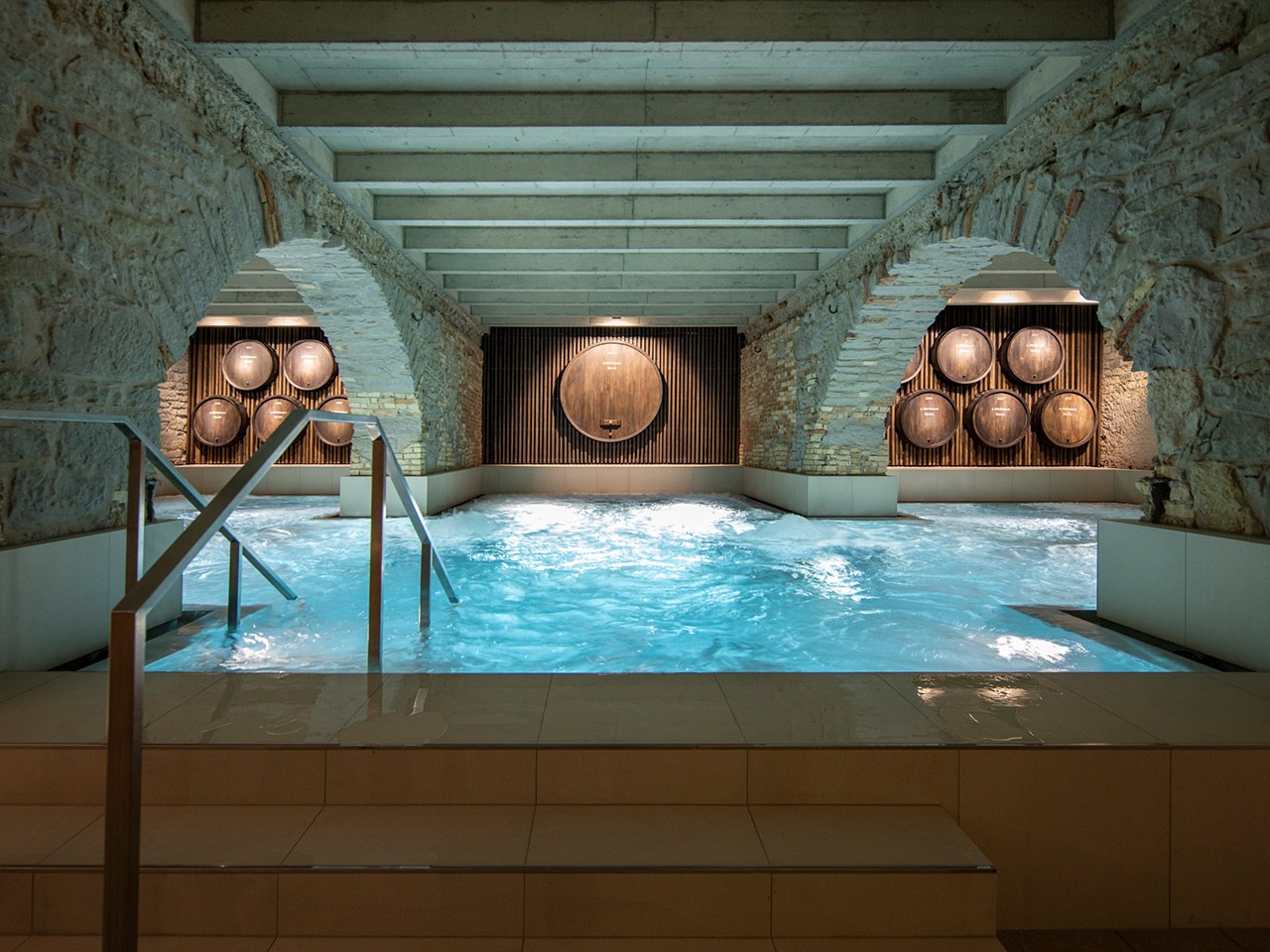 A glowing thermal pool beneath stone arches and old wooden beer barrels at Thermalbad & Spa Zurich