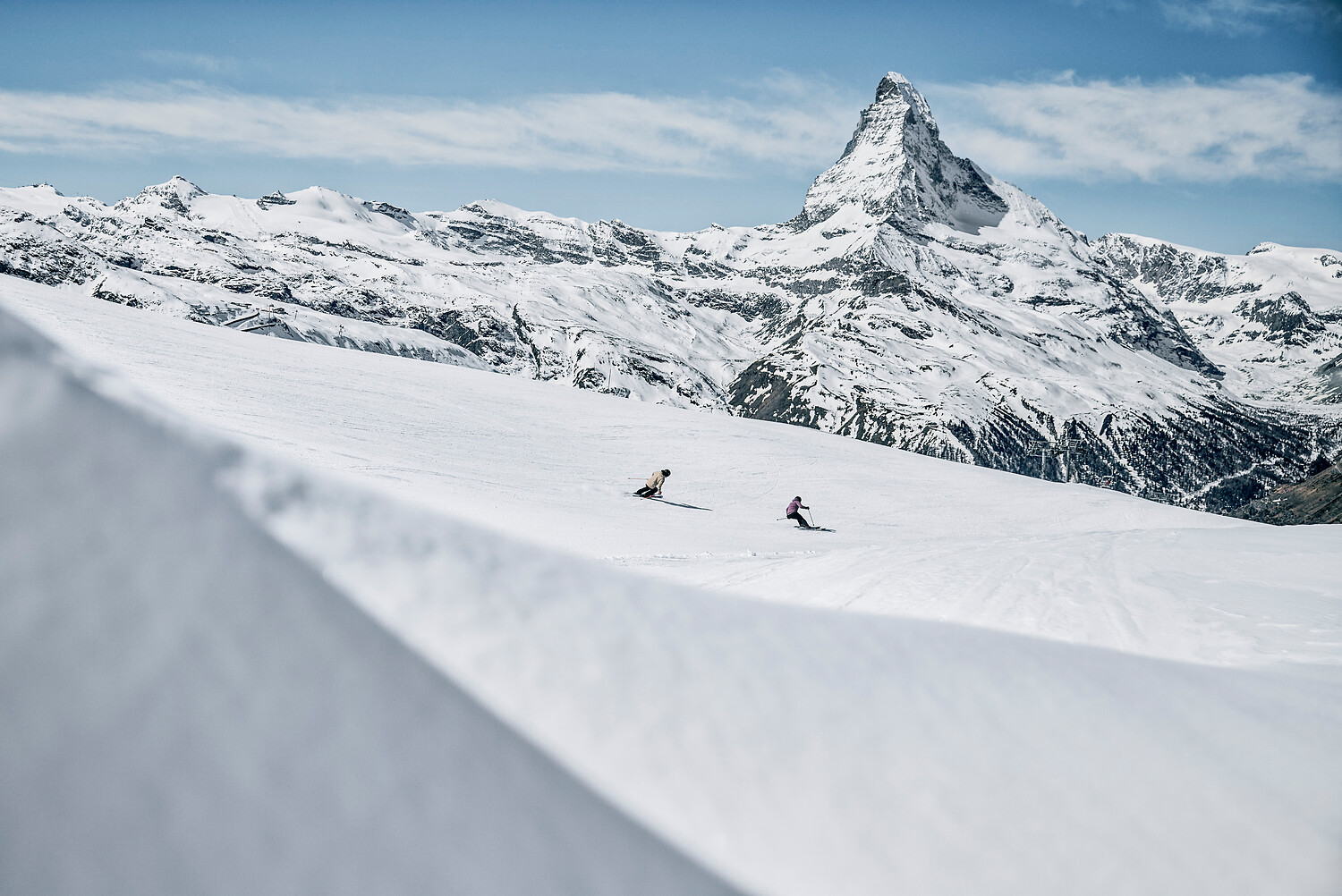 Two skiers on a wide, empty piste with the Matterhorn behind